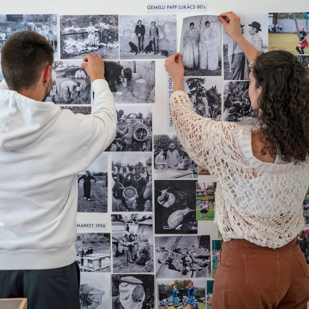 Due studenti appendono fotografie in bianco e nero su una parete di riferimenti